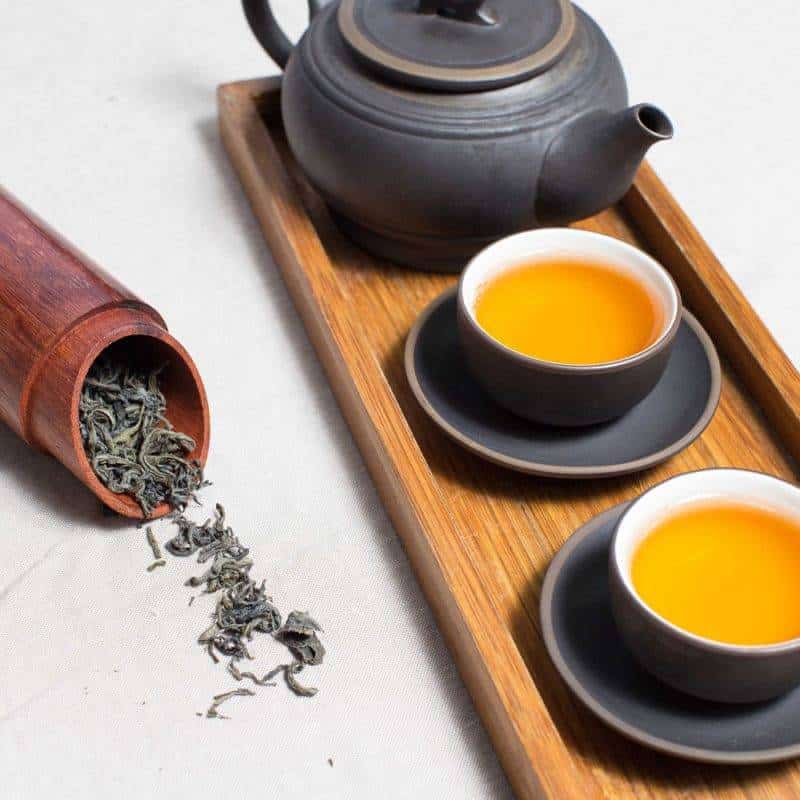plateau rectangle en bois avec deux tasses de thé pleine et une théillère noire avec du thé en vrac