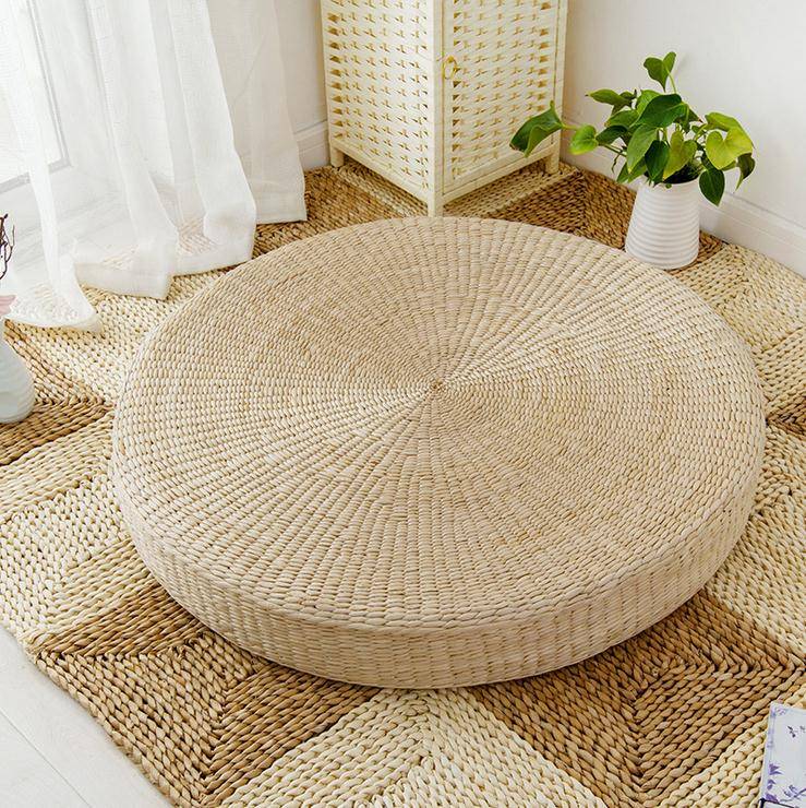 coussin tatami plat et rond en osier posé sur le sol à côté d'une plante et de rideau blanc