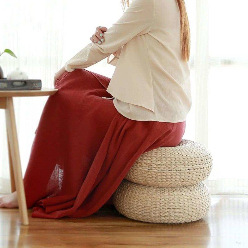femme avec une jupe longue rouge et un haut blanc assise sur deux coussins plat et rond tressés