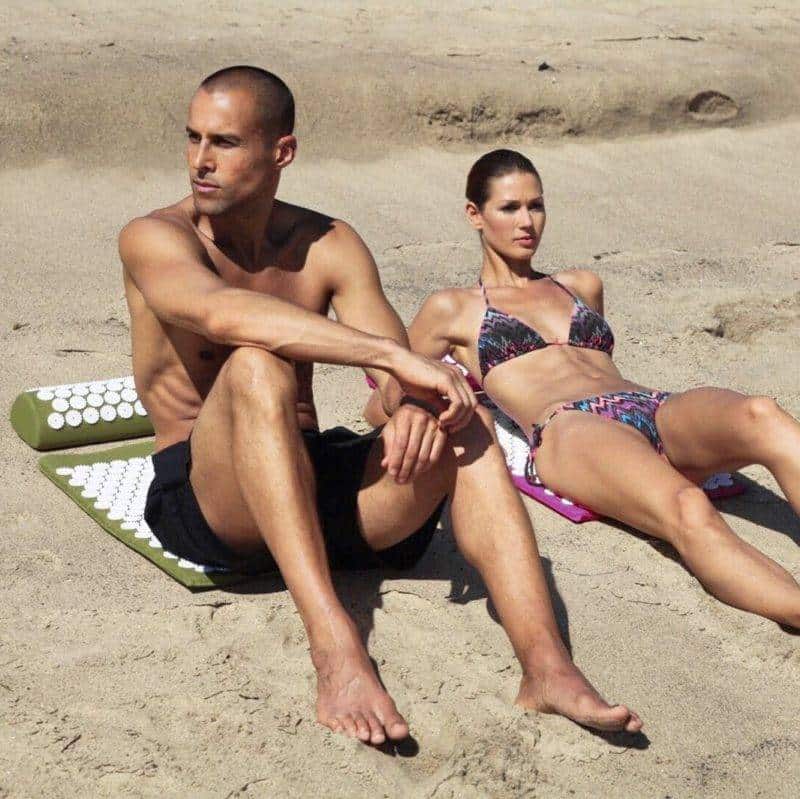 un homme et une femme en maillot de bain à la plage allongés sur deux tapis d'acupression