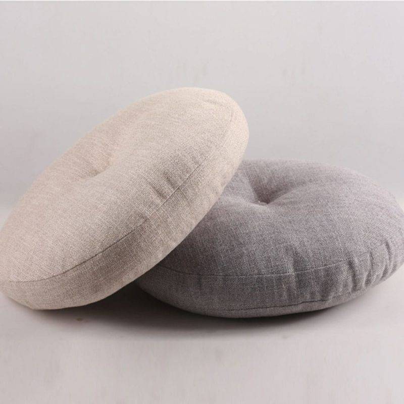 deux coussins beige et gris ronds superposé avec une pression au centre posés sur le sol