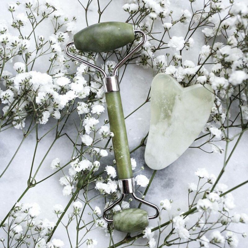 rouleau de jade vert posé sur des fleurs blanches avec une pierre de guasha