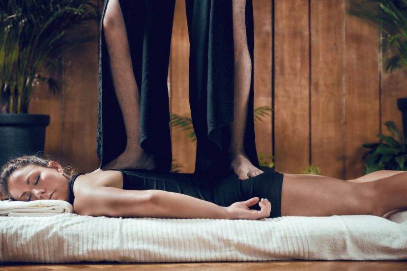 Belle jeune femme sportive profitant d'un massage du dos shiatsu, allongée sur le sol, portant des vêtements noirs