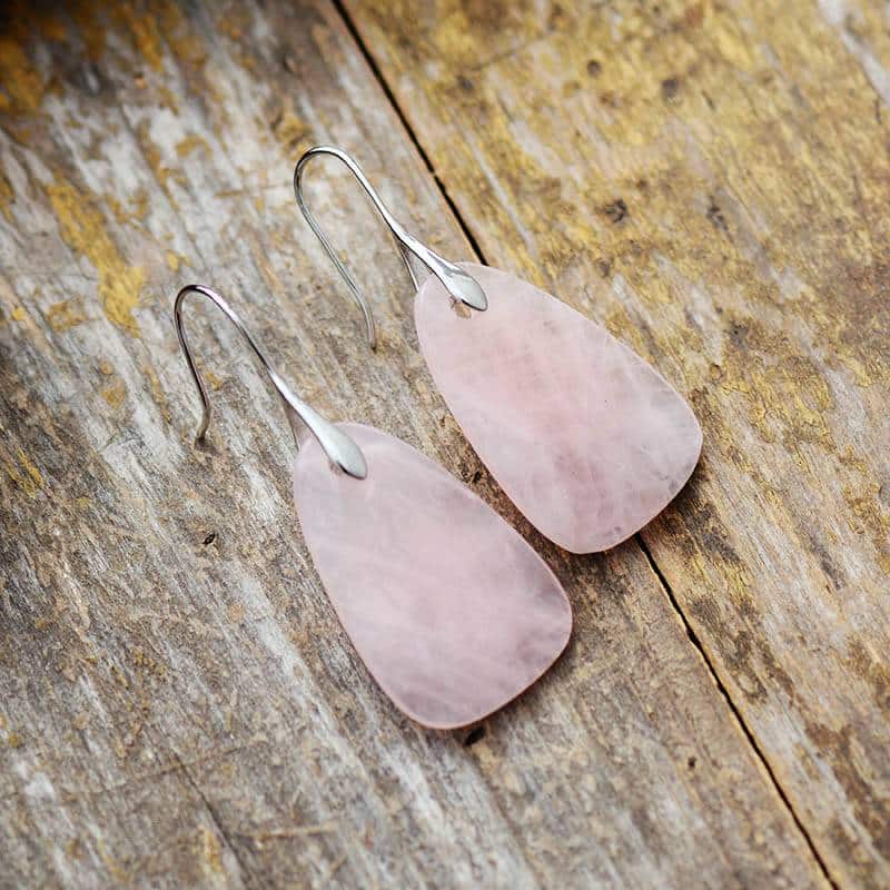 paire de boucles d'oreilles plaque en pierre rose quartz avec fermoir argent posé sur un support en bois