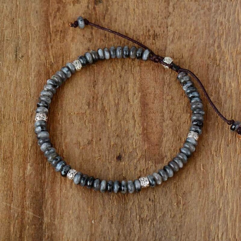 fin bracelet en petites pierres en forme de billes grises et blanche sur un fond en bois