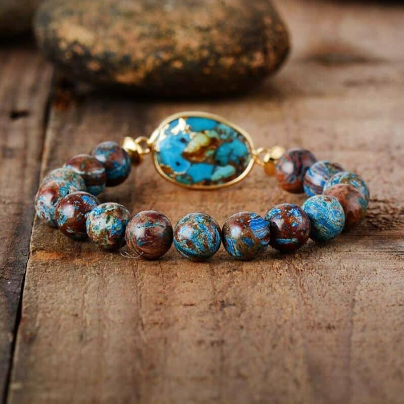 bracelet en pierres rondes bleu et marron avec grosse pierre ovale bleu et marron sur un cadre or sur fond en bois