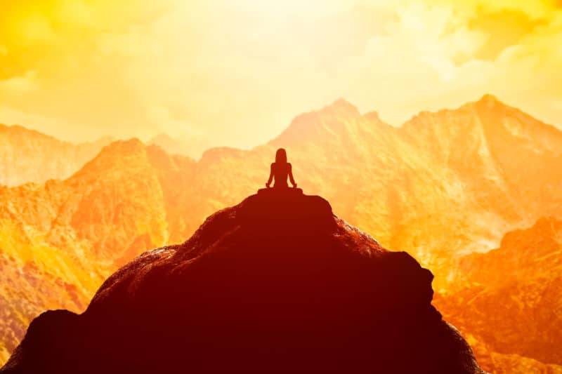 Femme méditant dans la position assise de yoga sur le sommet d'une montagne au-dessus des nuages