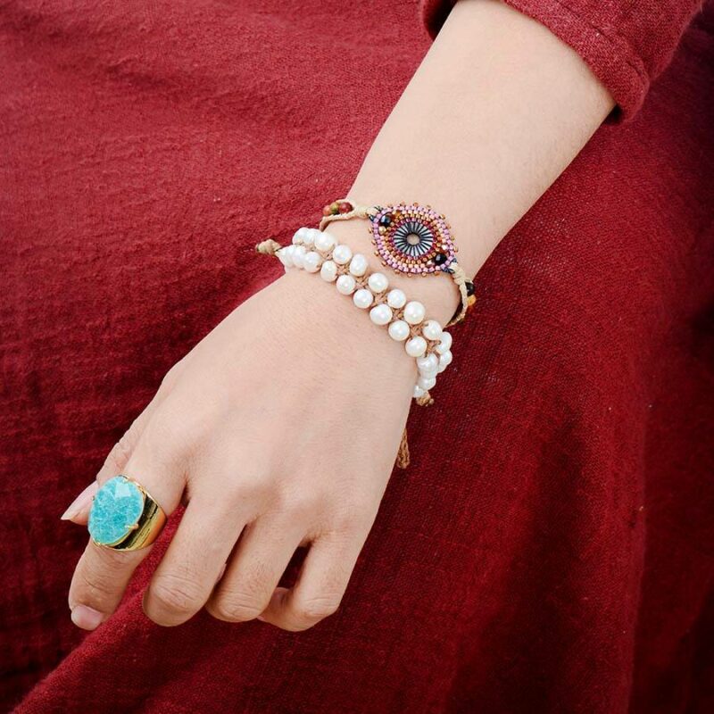 main portant une grosse bague en pierre turquoise amazonite avec des bracelets en perle et une robe rouge