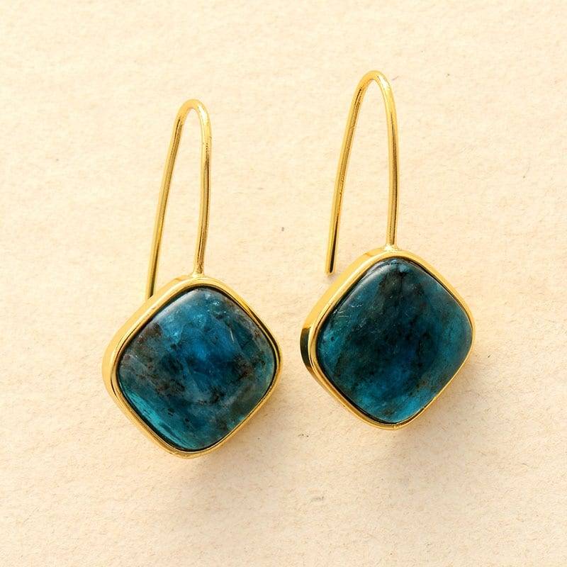 pare de boucles d'oreilles en pierre bleue avec monture dorée sur fond beige