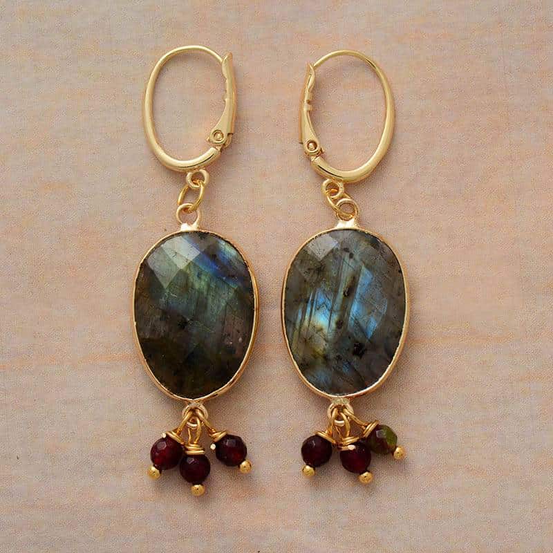 paire de boucles d'oreilles avec pierre ovale en labradorite et trois petites perles en pierre pendantes le tout sur une monture dorée et sur fond beige