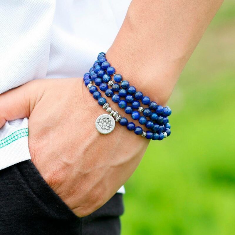 bracelet collier type chapelet en billes de pierre couleur bleue avec médaillon rond lotus enroulé autour d'un poignet avec une main dans les poches