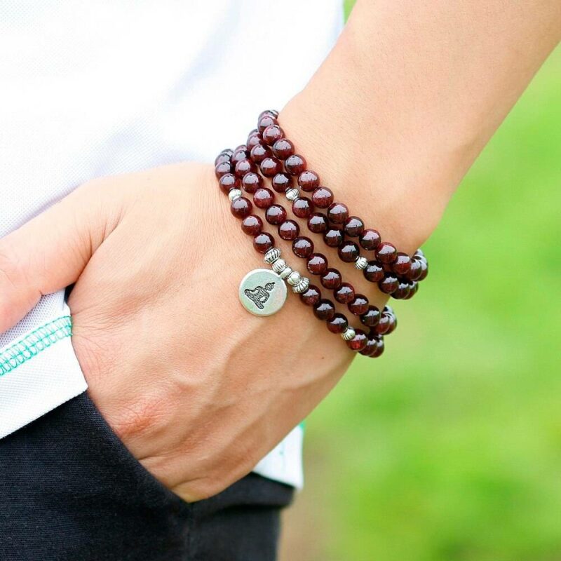 bracelet collier type chapelet en billes de pierre couleur marron avec médaillon rond bouddha enroulé autour d'un poignet avec une main dans les poches