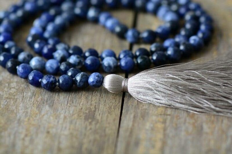 bracelet en perles bleu foncé avec un pompon gris posé sur du bois