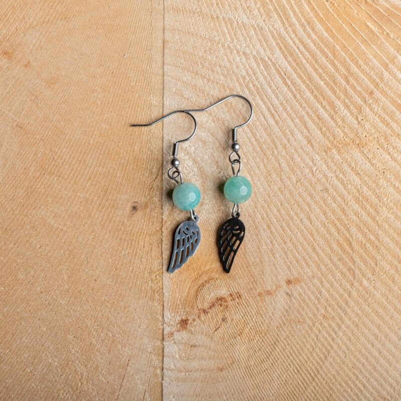 paire de boucle d'oreille pendante avec une pierre en forme de perle bleu et une aile argent sur fond bois