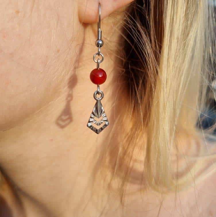 femme blonde portant une boucle d'oreille pendante avec une pierre en forme de perle rouge claire et un pendentif argent
