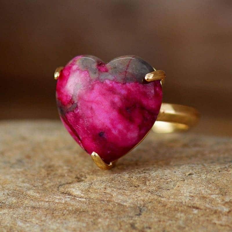 fine bague en or avec une pierre en forme de coeur rose posé sur une table
