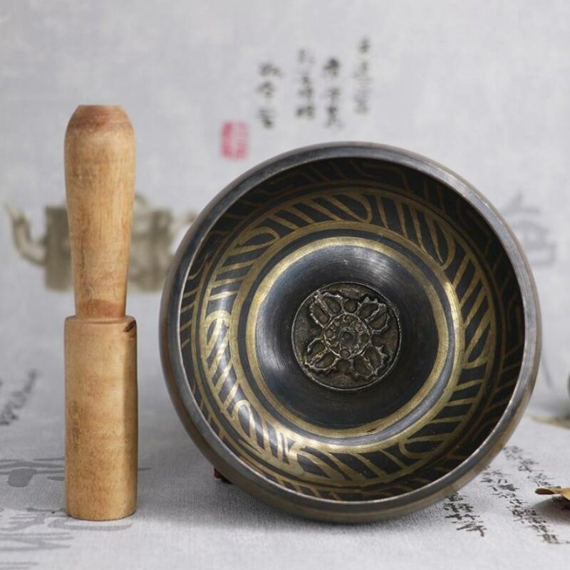 bol chantant tibétain noir et doré avec un pilon en bois sur un fond blanc avec des écritures japonaises
