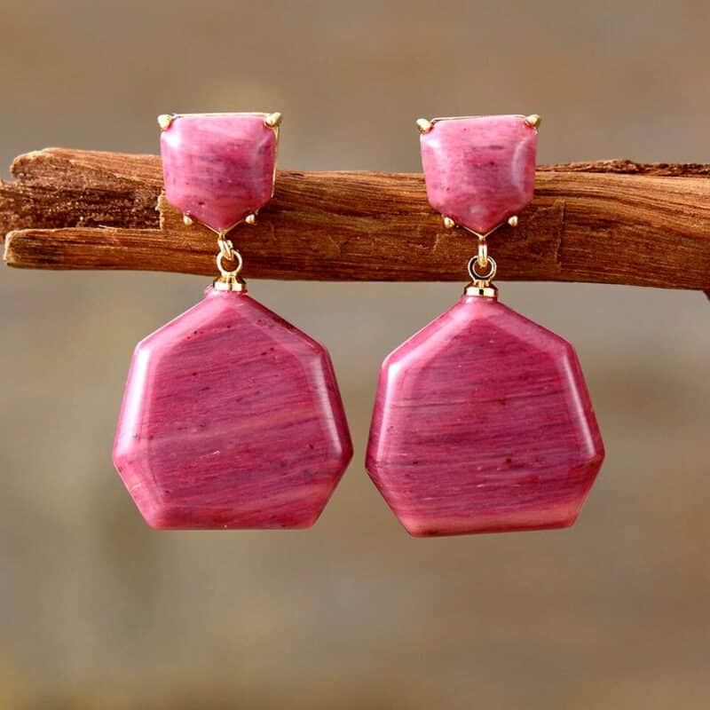 paire de boucles d'oreilles avec une grosse et une petite pierre rose fushia sur monture dorée accrochées à une branche