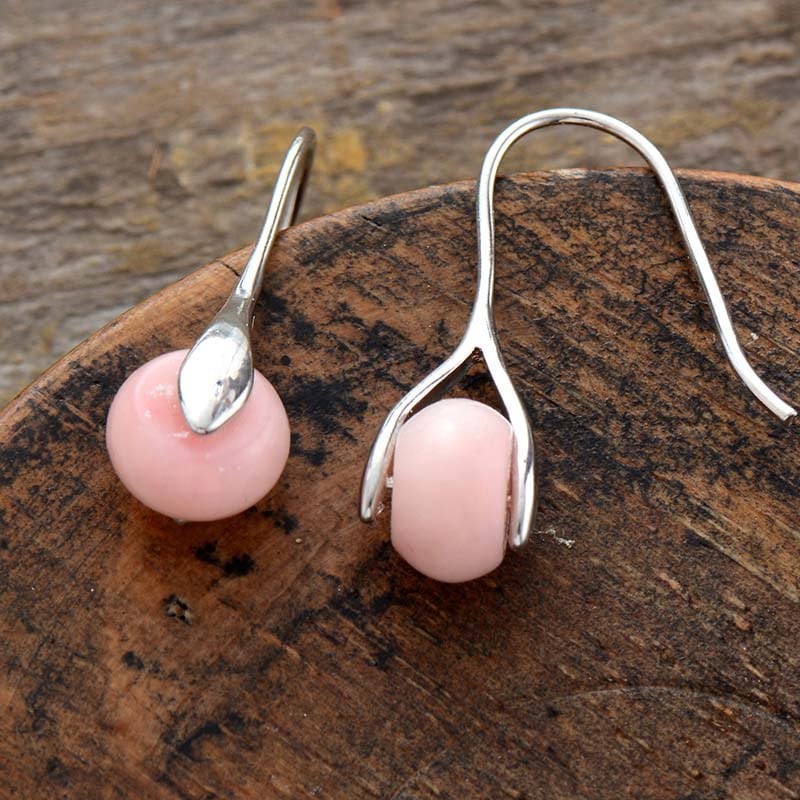 paire de boucles d'oreilles monture argent avec perle en pierre rose qui tourne posé sur du bois