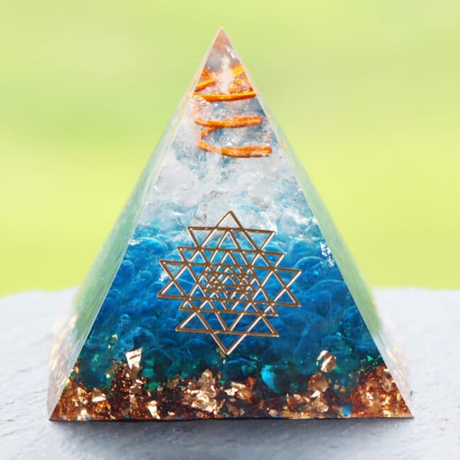 Accessoire ésotérique pyramide d'orgonite avec gravier de verre bleu sur fond vert et gris