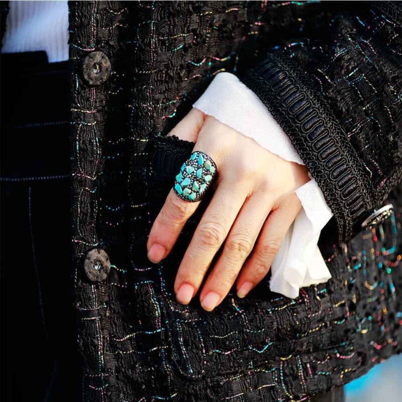main portant une bague en pierre bleu hematite sur un manteau noir