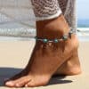 Bracelet de cheville à formes rondes avec perles de turquoise sur une cheville en fond de plage