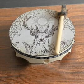 Tambour Chamanique Circulaire au Motif de Cerf avec un bâton posé sur une table en bois