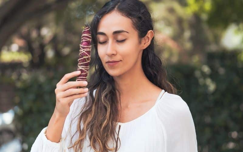 Femme portant un petit fagot de sauge rose devant son visage, les yeux fermés