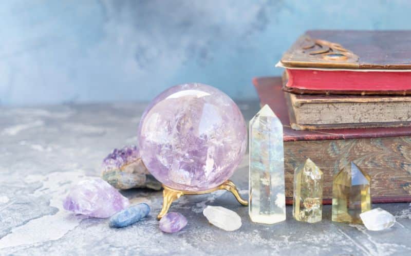 Pile de 3 livres, à côté se trouve des pierres minérales sous différentes forme, une boule, des pierres polies et des pierres taillées.