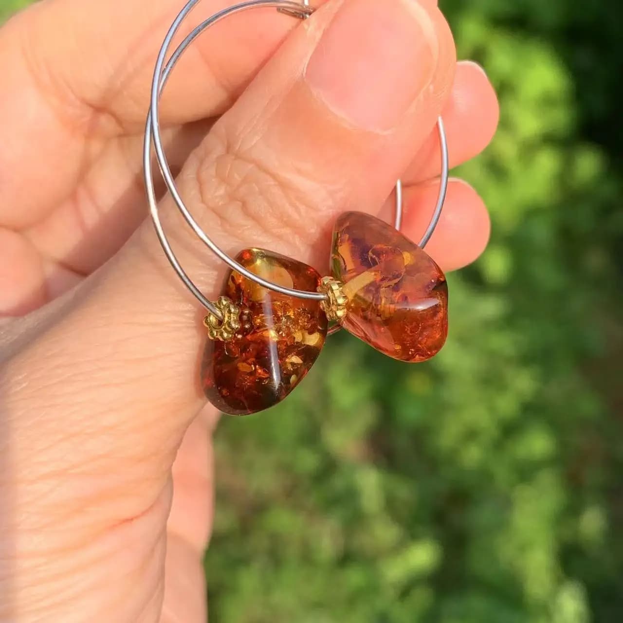 Boucles d'Oreilles Ambre Rondes dans les mains d'une personne sur fond vert