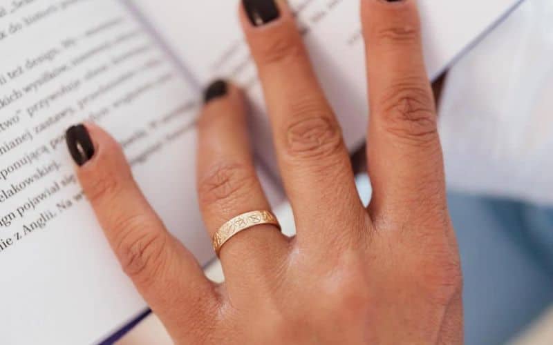 Main d'une femme portant un anneau bague celtique en or doré, les doigts posés sur un livre ouvert.